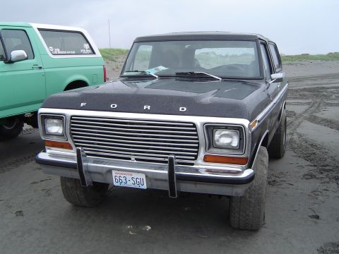 1989 Ford Bronco - A black Ford Bronco is parked on a sandy beach next to a green Bronco, with a Washington license plate visible on the front.
