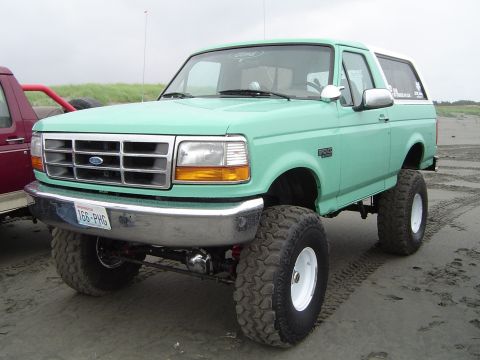 1989 Ford Bronco - This lifted 1989 Ford Bronco is parked on a beach next to another vehicle.