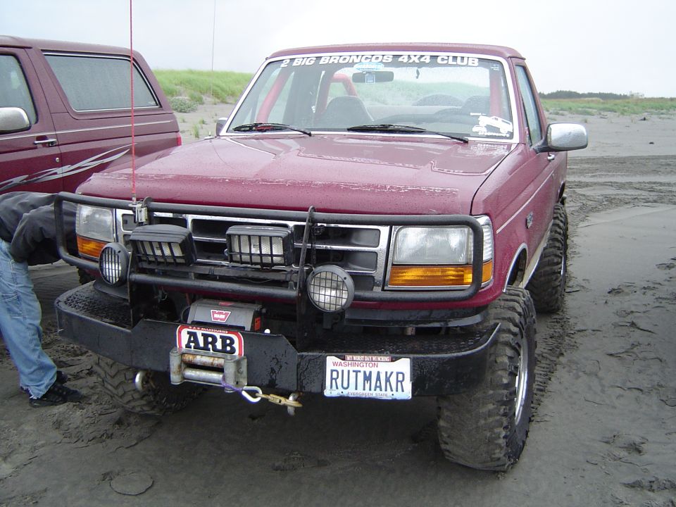 Lifted maroon Ford Bronco with ARB bumper and Warn winch on a wet beach