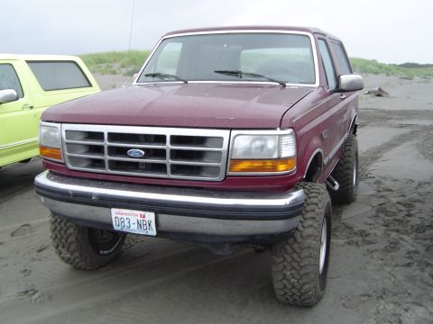 1989 Ford Bronco - A maroon Ford Bronco with a lifted suspension sits on a sandy beach next to a yellow vehicle.
