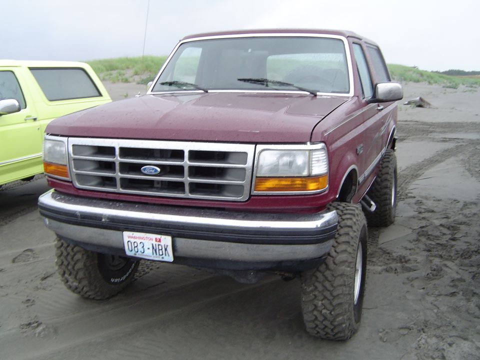 Maroon Ford Bronco on beach, front view, lifted suspension, large tires, Washington license plate 083-NBK