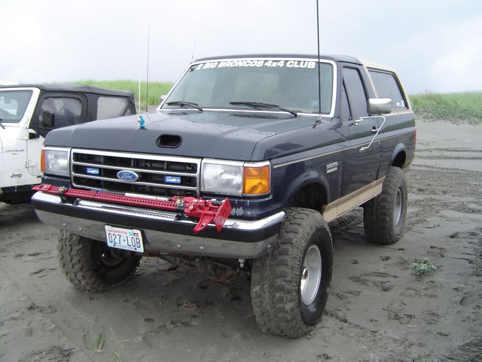 Dark blue 1989 Ford Bronco with off-road tires and Hi-Lift jack. "BIG BRONCOS 4x4 CLUB" sticker on windshield
