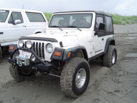 1989 Ford Bronco - White Jeep Wrangler and Ford Bronco on a sandy beach under an overcast sky.