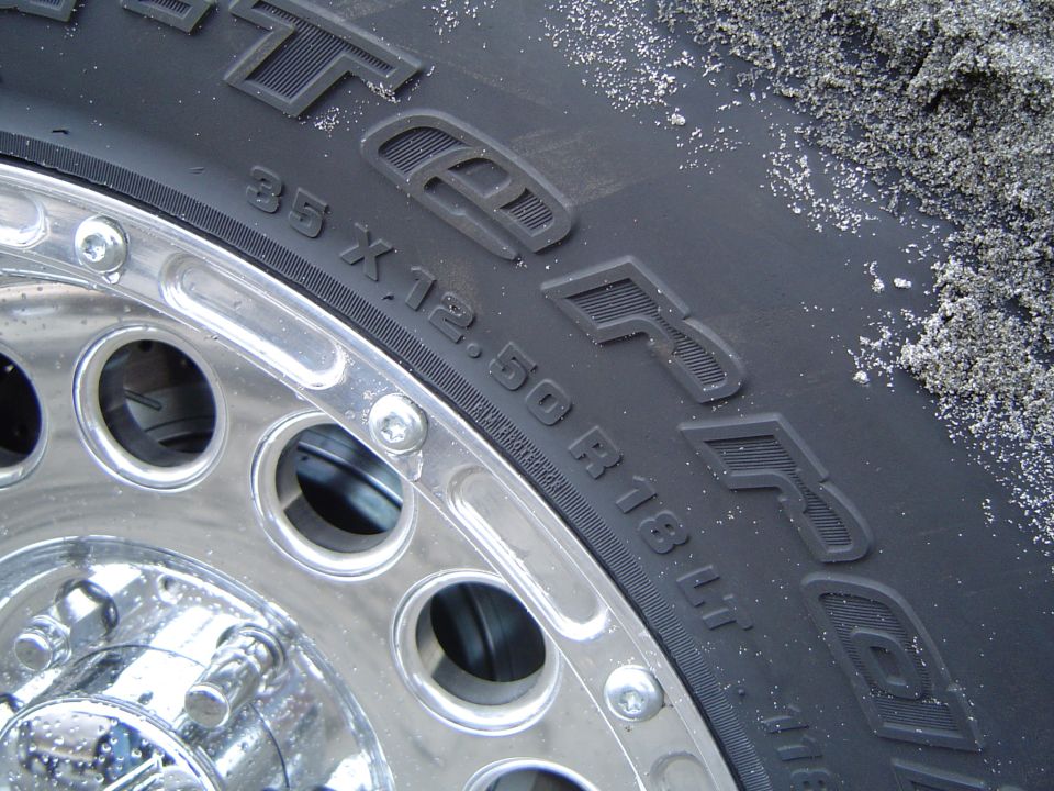 Close-up of a 35x12.50R18LT tire sidewall on a polished alloy wheel with sand on the tread