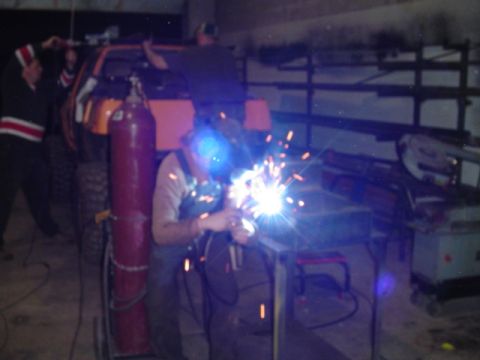 1993 Ford Bronco - A person is welding in a garage, with an orange vehicle and a red gas tank visible in the background.