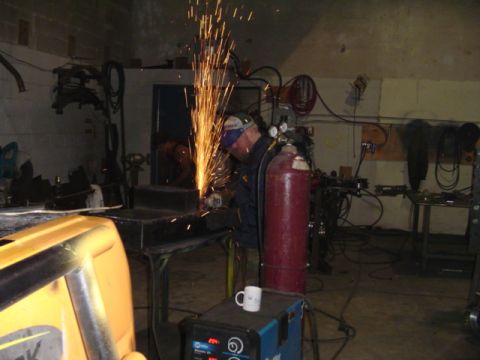 1993 Ford Bronco - A worker uses a grinder to create sparks while working in a garage setting with welding equipment.