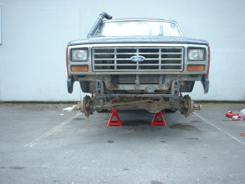1983 Ford Bronco - The front end of a Ford truck is elevated on jack stands, revealing its suspension and chassis components.