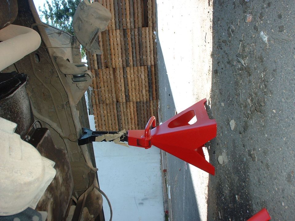 Red jack stand supporting a vehicle frame, with wooden planks in background