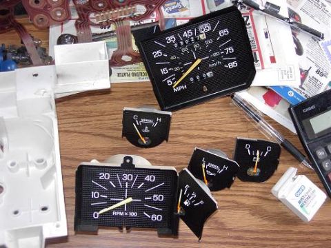 1980 Ford Bronco - A collection of dashboard gauges and parts, including a speedometer and tachometer, are laid out on a wooden surface.