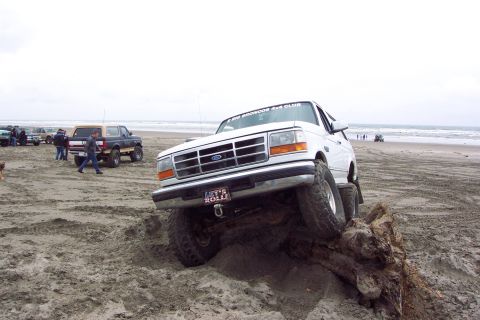 1996 Ford Bronco - A white Ford Bronco navigates a sandy beach, with other vehicles and people in the background.