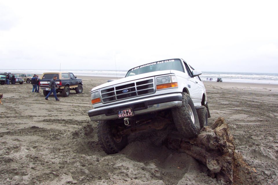 White lifted Ford Bronco climbing driftwood log on a sandy beach