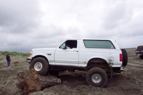 1996 Ford Bronco - A white 1996 Ford Bronco navigates a sandy, off-road environment with another vehicle visible in the background.