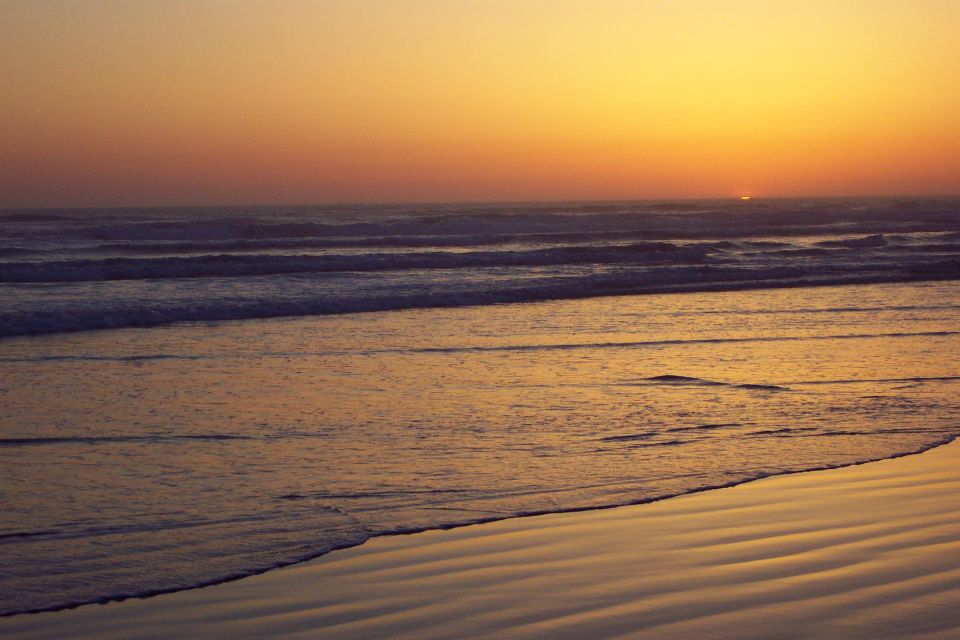 Ocean sunset with orange and pink sky over waves and a wet reflective beach