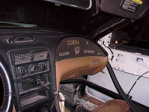 1995 Ford Mustang - The interior of a modified car shows a roll cage and custom dashboard text.
