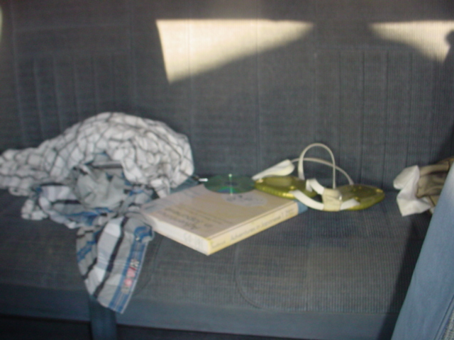 Gray cloth bench seat holding a book, two green discs and a crumpled plaid garment