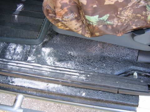 1992 Ford Bronco - Close-up of the interior floor and seat bottom, showing a textured coating and a camouflage seat cover.