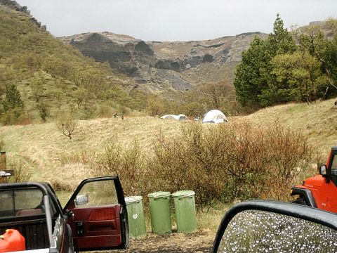 1996 Ford Bronco - A campsite is set up in a hilly area, with several tents visible in the distance and vehicles parked nearby.