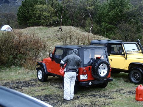 1996 Ford Bronco - Two off-road vehicles, a red Jeep and a yellow Land Rover, are parked on a grassy area with tents in the background.