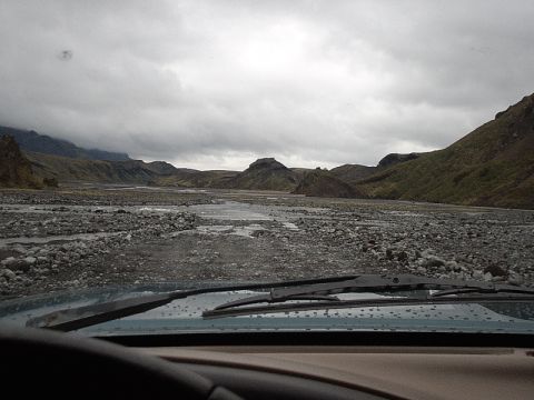 1996 Ford Bronco - Driving through a rocky riverbed with a view of mountains and a cloudy sky.