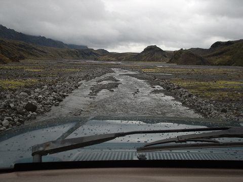 1996 Ford Bronco - View from inside a vehicle driving through a rocky, wet landscape with mountains in the distance.