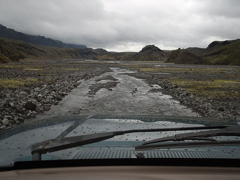 POV from inside vehicle crossing a rocky river valley through a wet windshield