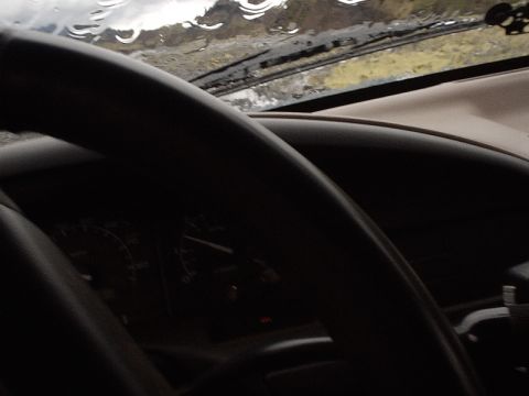 1996 Ford Bronco - Interior view of a 1996 Ford Bronco, showing the dashboard and steering wheel with a rain-streaked windshield.
