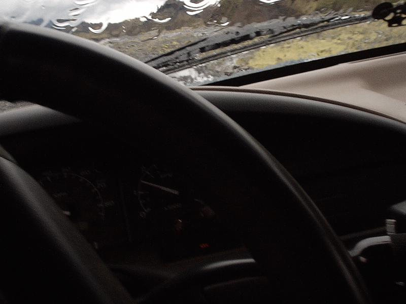 Driver's view through steering wheel showing gauges and rainy windshield