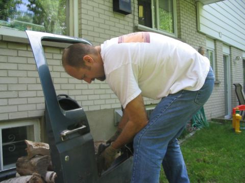 1986 Ford Bronco - A man works on a detached car door in a residential yard.