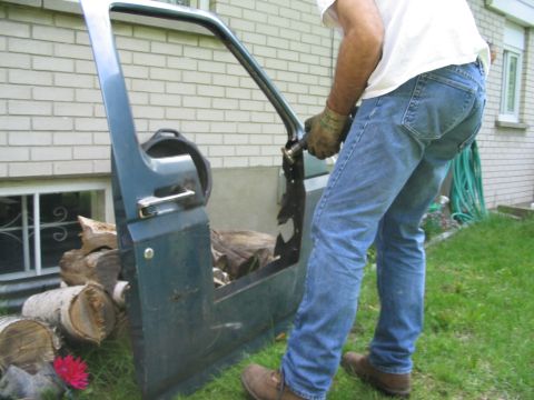 1986 Ford Bronco - A person removes a dark green vehicle door, revealing the internal frame and hardware.