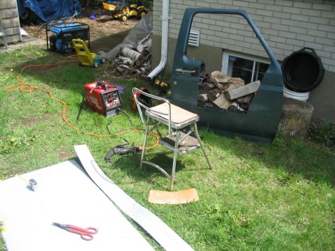 1986 Ford Bronco - A detached vehicle door is being used to store firewood in a grassy yard.