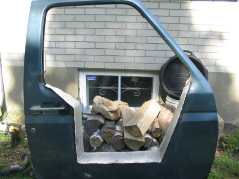 1986 Ford Bronco - A car door filled with firewood sits outside a brick building.