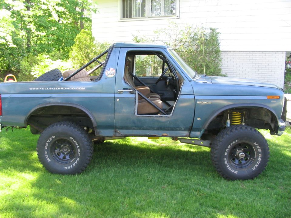 Lifted teal Ford Bronco on grass with half doors, no top, roll cage and mud tires