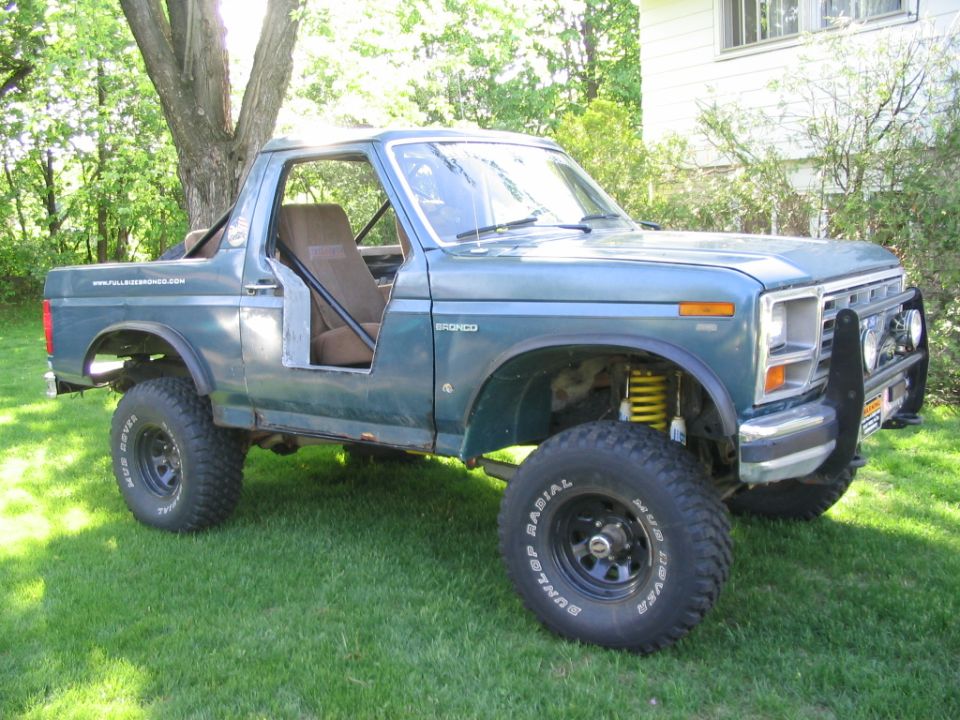 Blue Ford Bronco, doors and top off, lifted on mud tires, parked on grass