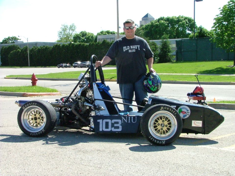 Black Formula SAE open-wheel car numbered 103 NIU with a person holding a helmet beside it
