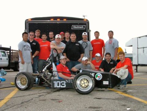 1985 Ford LTD Crown Victoria - NIU Formula SAE team poses in a parking lot behind their open-wheel race car numbered 103, which wears NIU lettering, gold mesh wheels and…