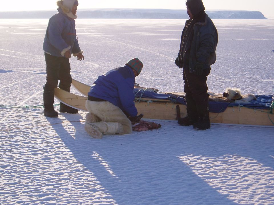 Three people in parkas around a wooden sled on arctic snow and ice