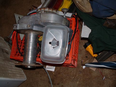1979 Ford Bronco - A winch spool and a metal engine part are resting on an orange crate, surrounded by other items.