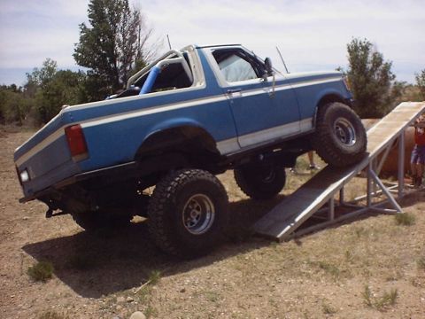 1988 Ford Bronco - A modified blue Ford Bronco with white racing stripes is positioned on an off-road ramp.