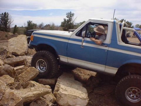 1988 Ford Bronco - A blue and white 1988 Ford Bronco navigates a rocky trail, with another vehicle visible in the background.