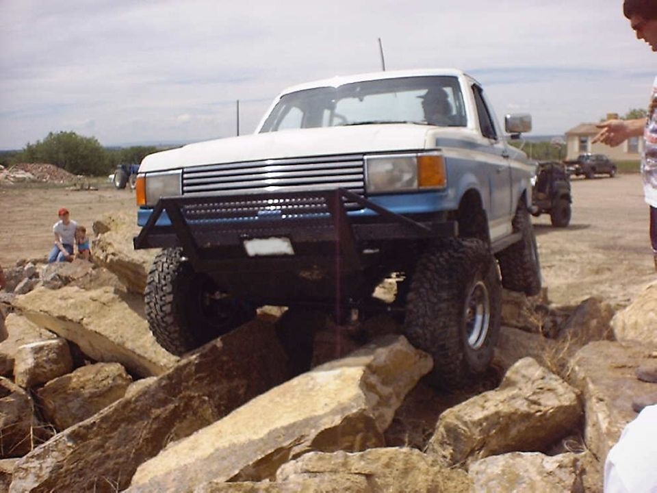 White and blue pickup truck with custom bumper navigating rocks