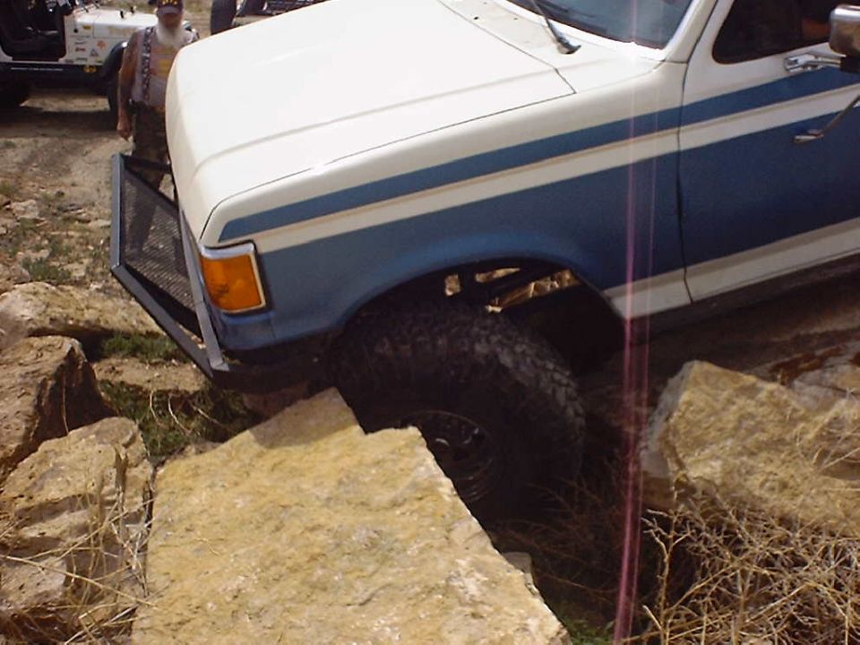 Ford Bronco with custom bull bar driving over rocks. Another Jeep is visible behind it