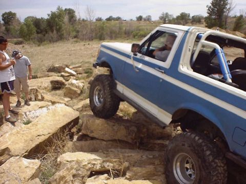1988 Ford Bronco - Ford Bronco navigating a rocky off-road course with two people watching.