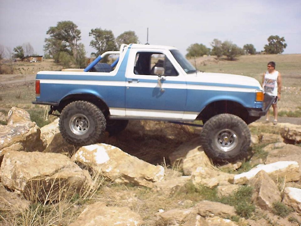 Blue and white 1987 Ford Bronco with lifted suspension navigating rocky terrain