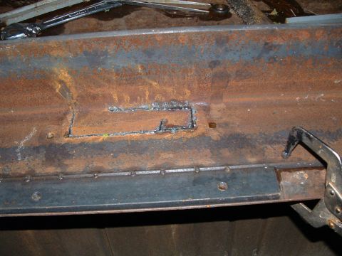 1979 Ford Bronco - Close-up of a rusty metal frame undergoing repair with welding and a clamp visible.
