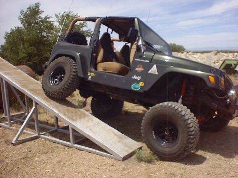1988 Ford Bronco - A green Jeep Wrangler is shown climbing a metal ramp during an off-road event.