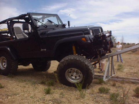 1988 Ford Bronco - A black Jeep Wrangler is positioned on a metal ramp during an off-road event.