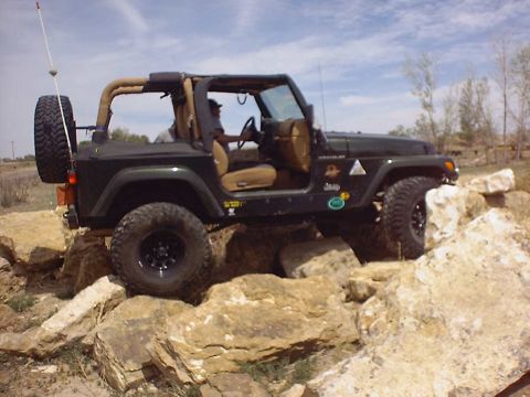 1988 Ford Bronco - A dark green Jeep Wrangler is shown traversing a challenging rocky obstacle course.