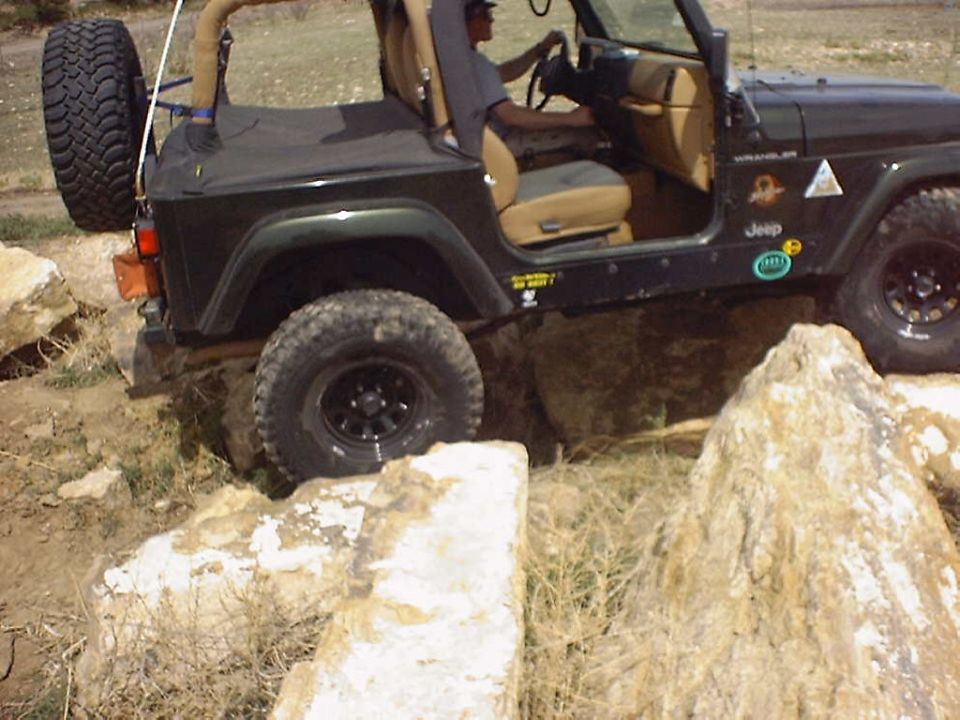 Jeep Wrangler with spare tire on back, driving over large rocks on a trail