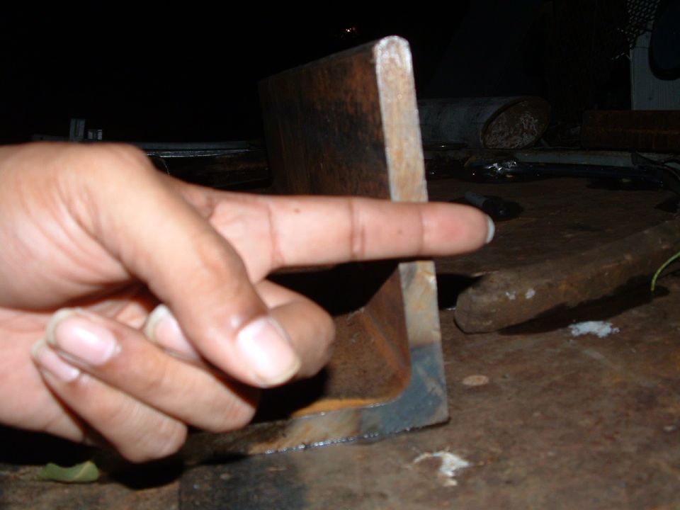 Hand pointing at a rusty metal angle bracket on a workbench