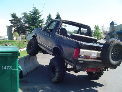 1993 Ford Bronco - A modified Ford Bronco is shown with its front wheels on a concrete barrier, demonstrating its off-road capabilities.